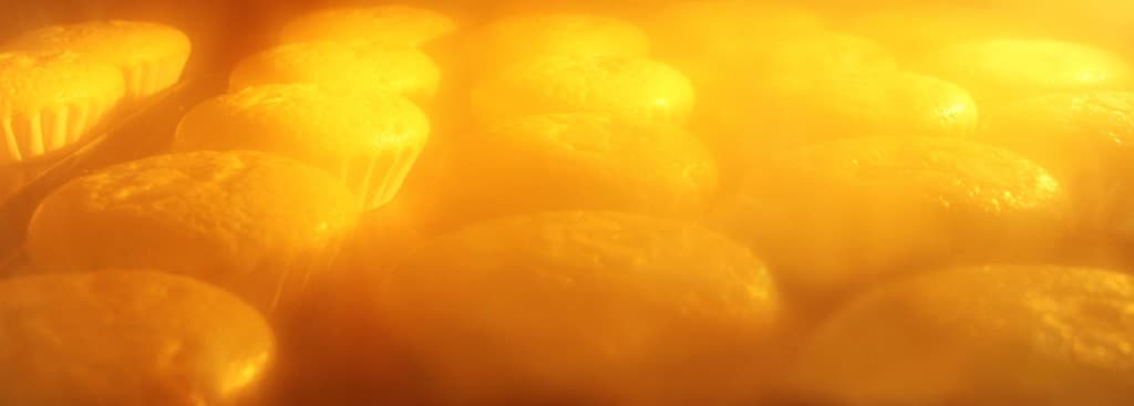 オーブン内で焼かれる小さなケーキやマフィン。オレンジ色の暖かい光に包まれた製菓の様子