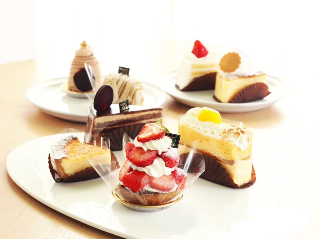 白い皿に並んだいちごのタルトやチョコレートケーキなど、季節の生ケーキのイメージ
